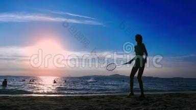 剪影。 人们在日落时在海滩上打羽毛球。